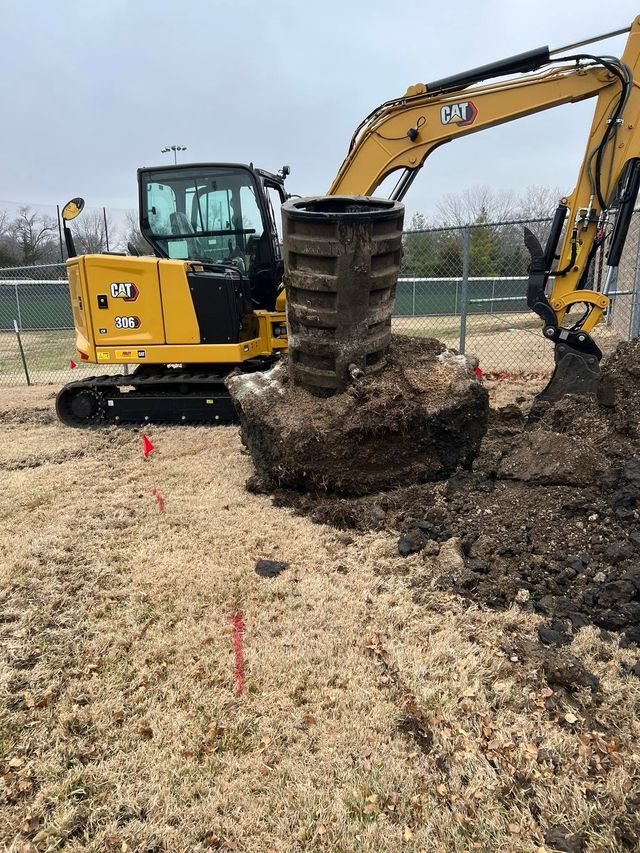 Yellow excavator lifting a tree root ball at a construction site with wood chips and gravel