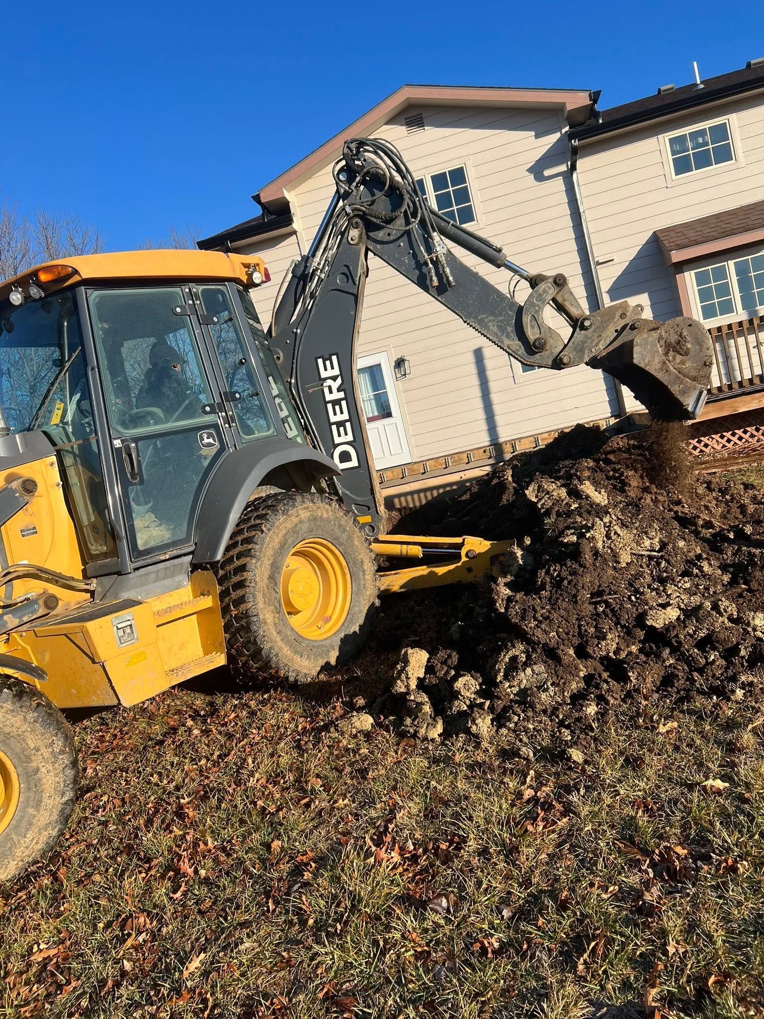 Yellow backhoe loader digging dirt beside a house on a sunny day