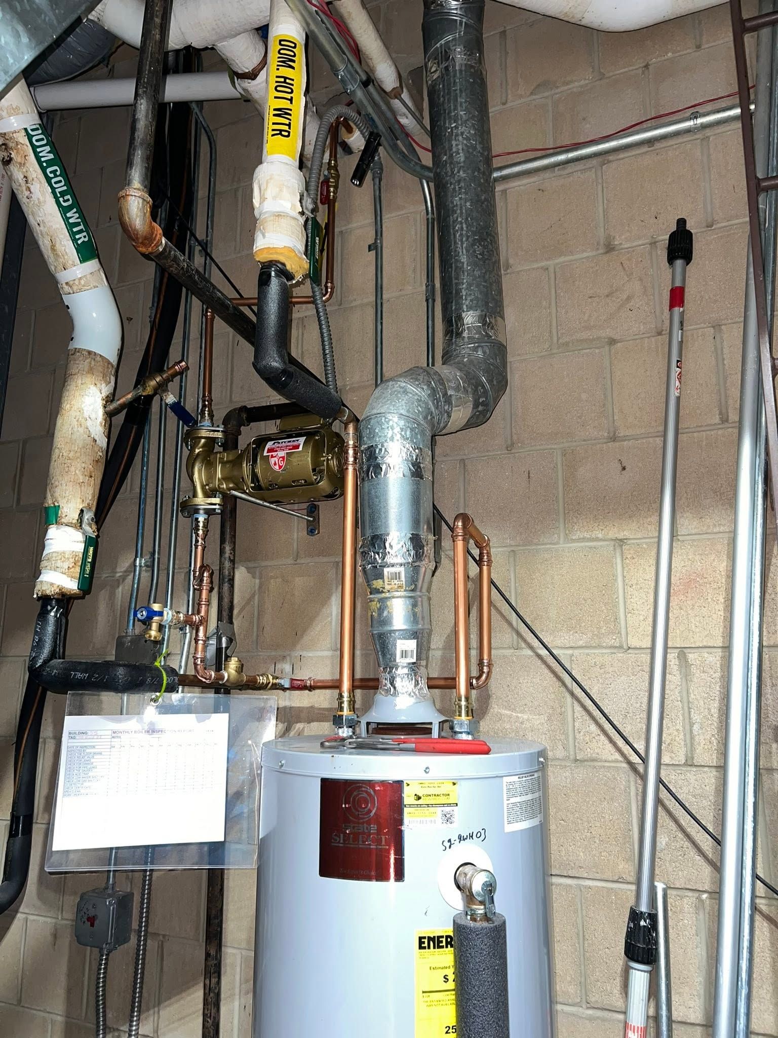Water heater with metal plumbing pipes, valves, and labels in a utility room.