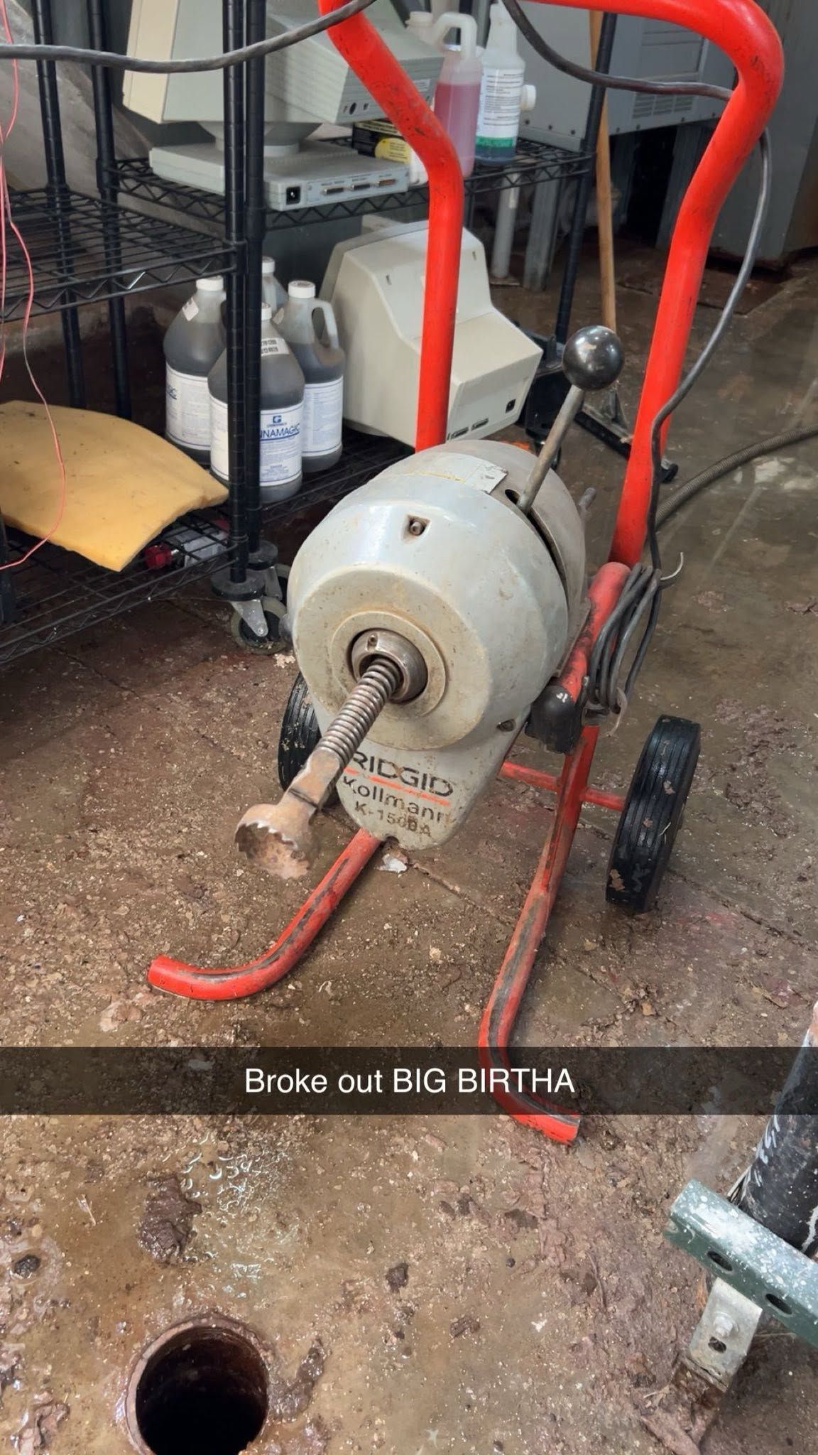 Red hand truck carrying a gray metal machine in a workshop, with scattered tools and a concrete floor.
