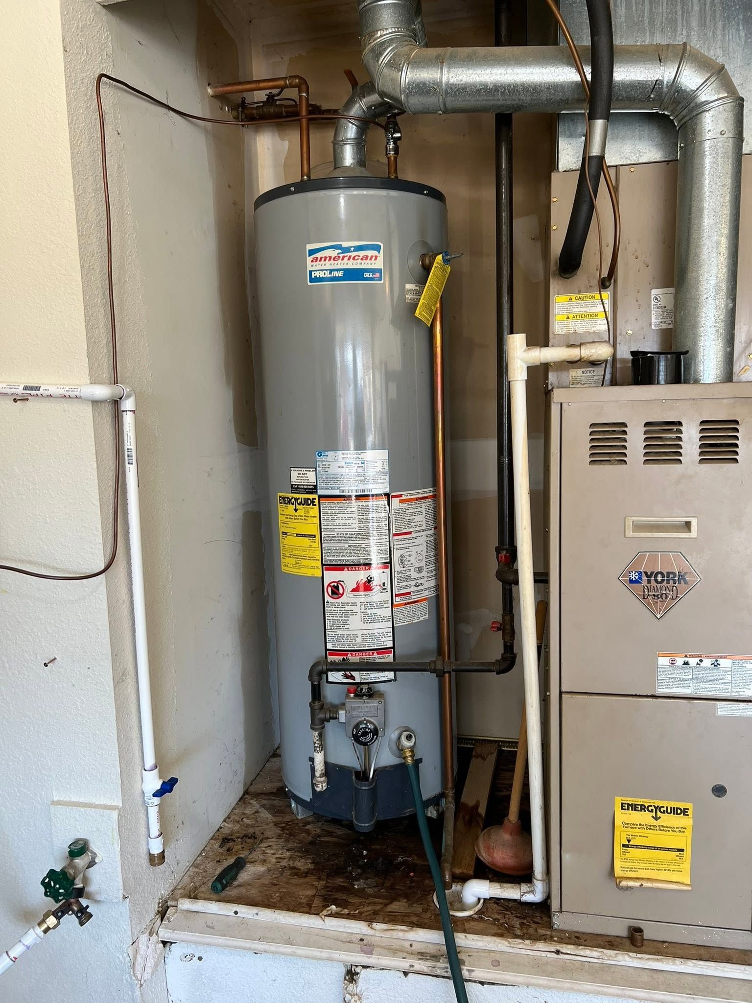 Water heater and furnace in a narrow utility closet with exposed pipes and a drain pan.