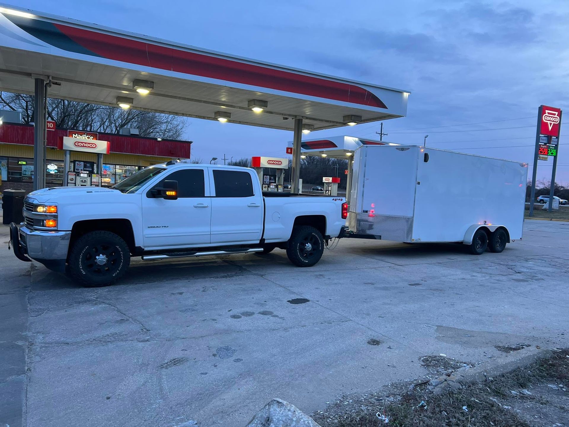 White pickup truck towing a white enclosed trailer at a gas station at dusk
