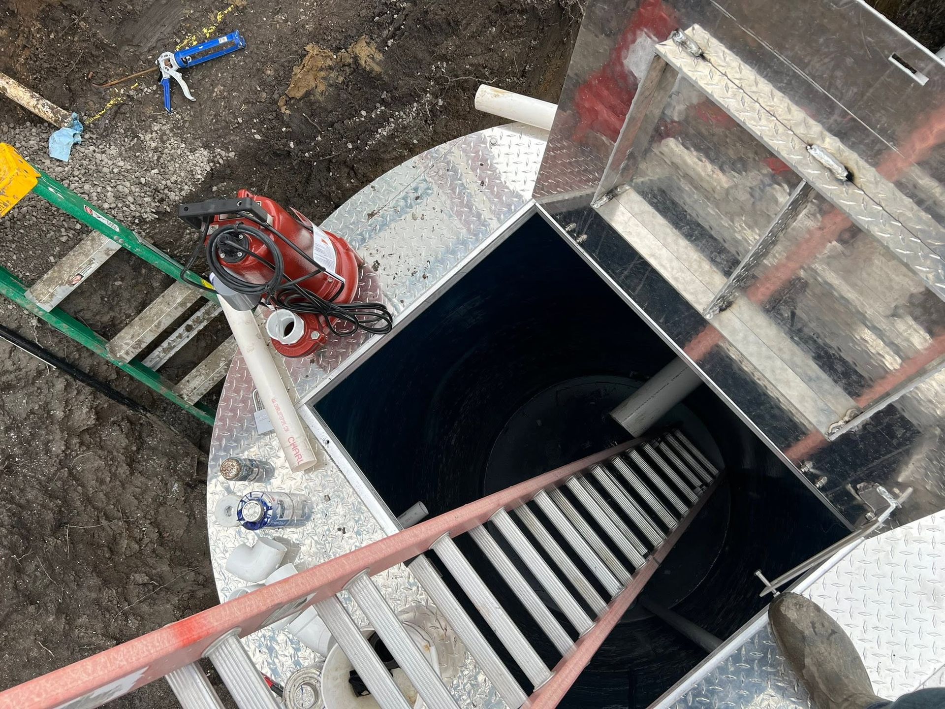 Open manhole with ladder, red tripod hoist, and construction tools around the shaft.