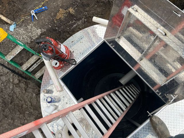 Open manhole with ladder, red tripod hoist, and construction tools around the shaft.