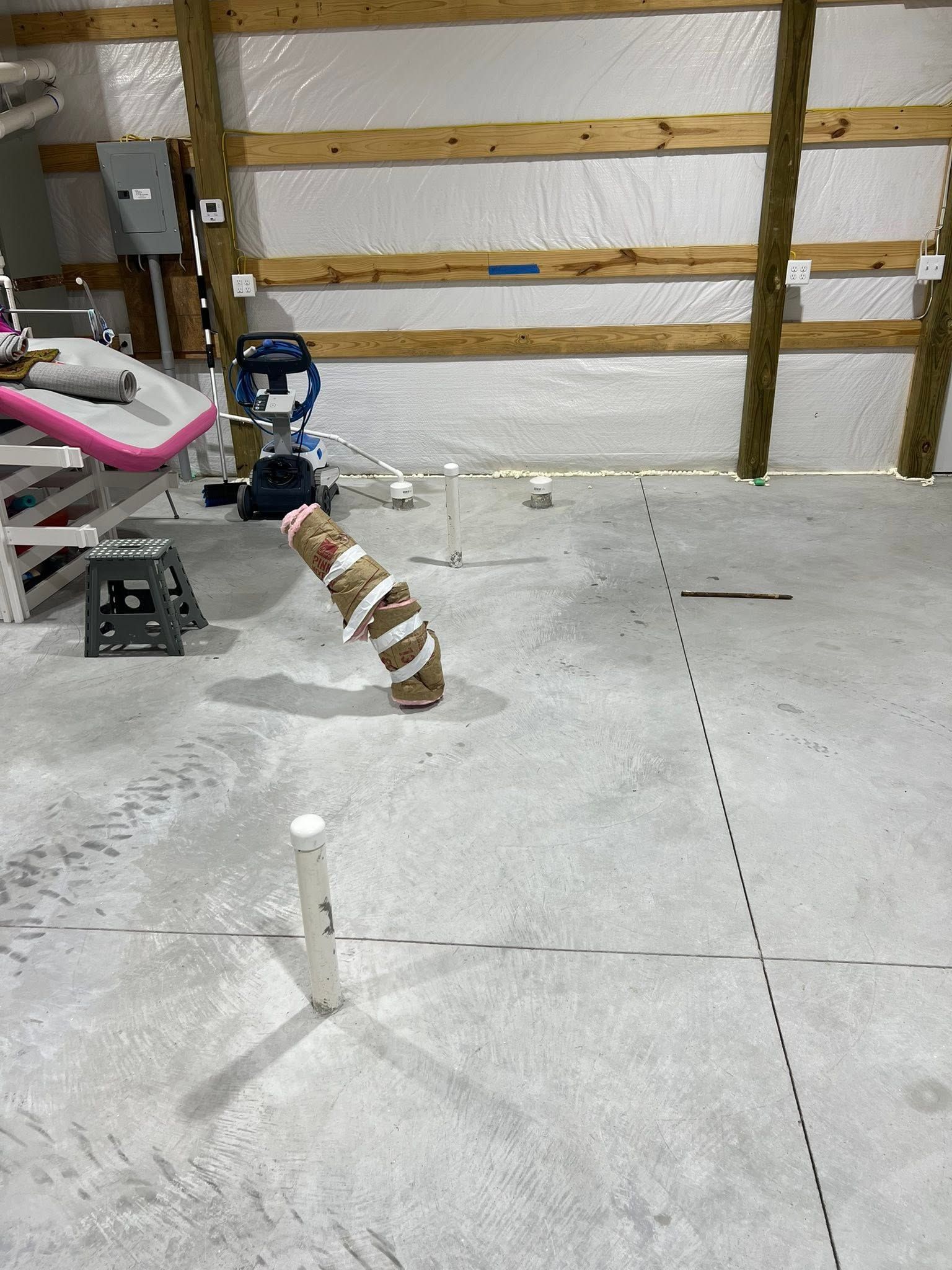Workshop floor with a small robot arm and a striped object near wooden wall studs