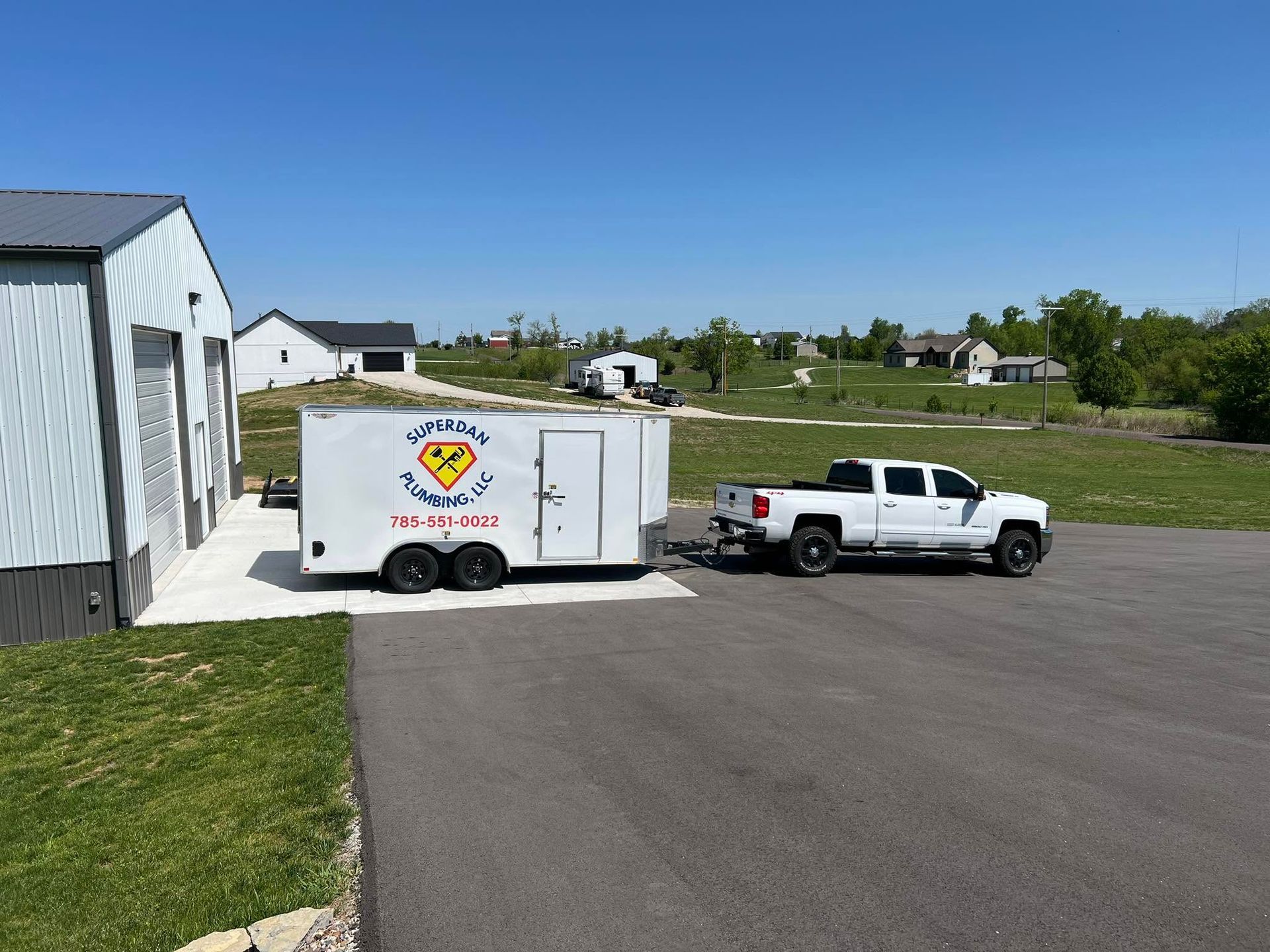 White pickup towing a white enclosed trailer beside a shed in a rural driveway under a blue sky