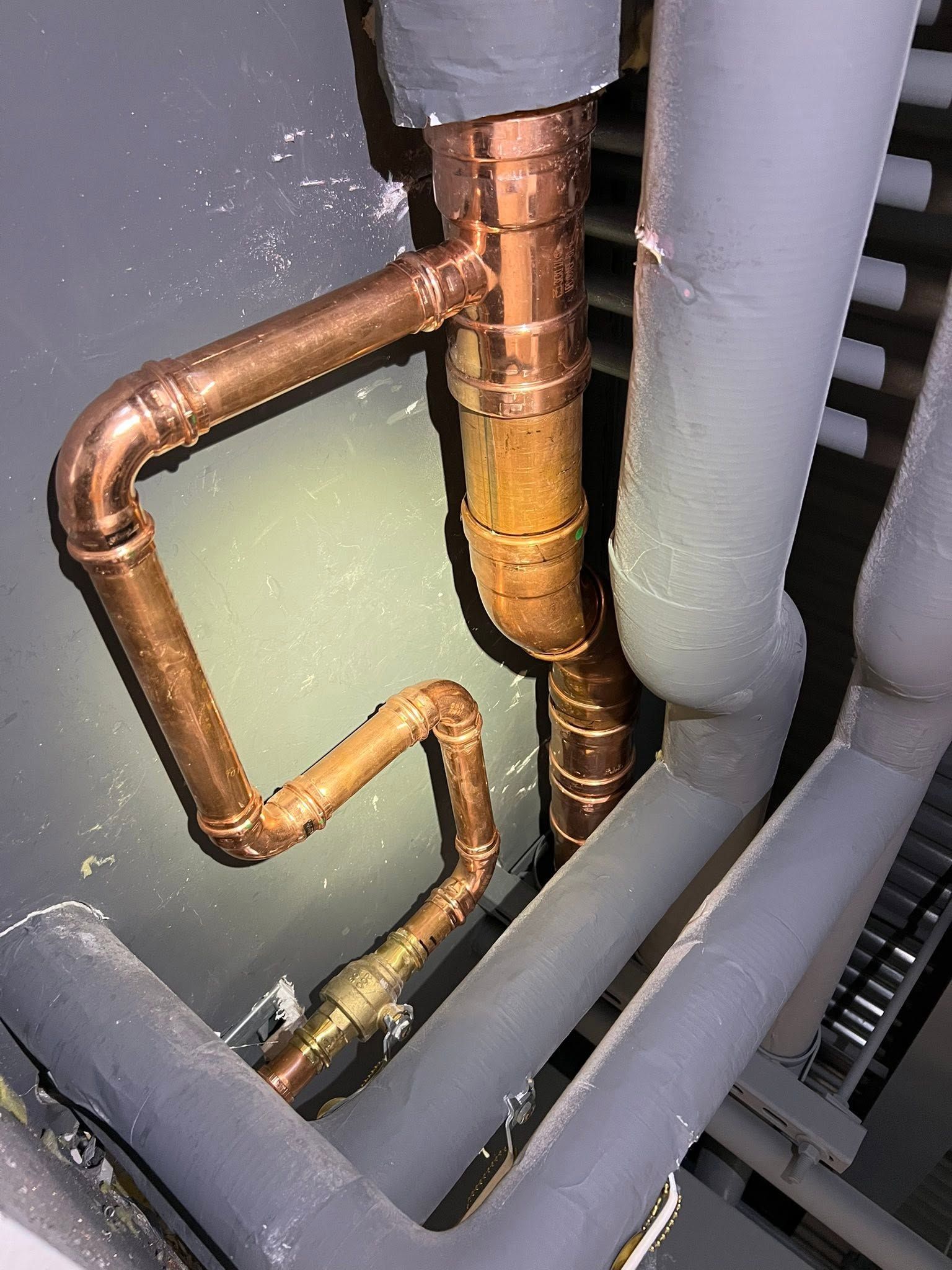 Copper and yellow insulated pipes in an industrial utility shaft beside gray ducts
