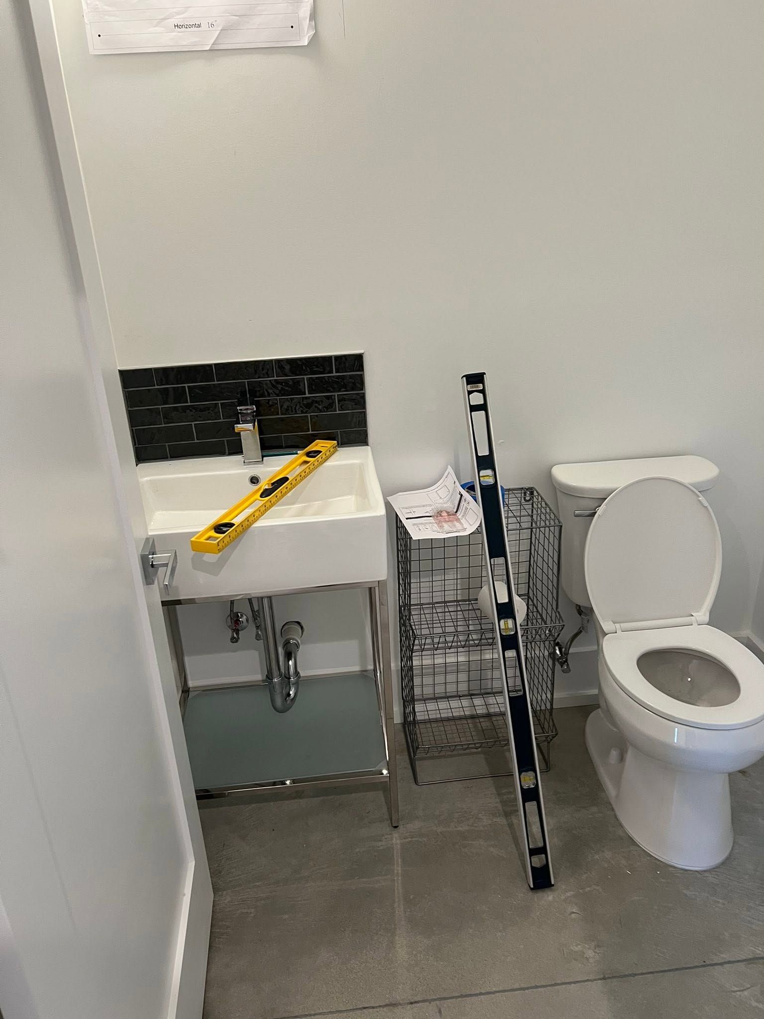 Small bathroom with sink, toilet, black shower chair, and a yellow grab bar across the sink.