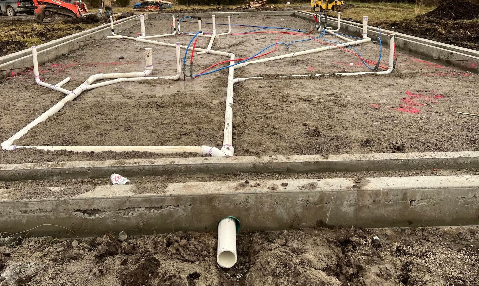 Plumbing foundation layout with white PVC pipes and trenches in a dirt construction site