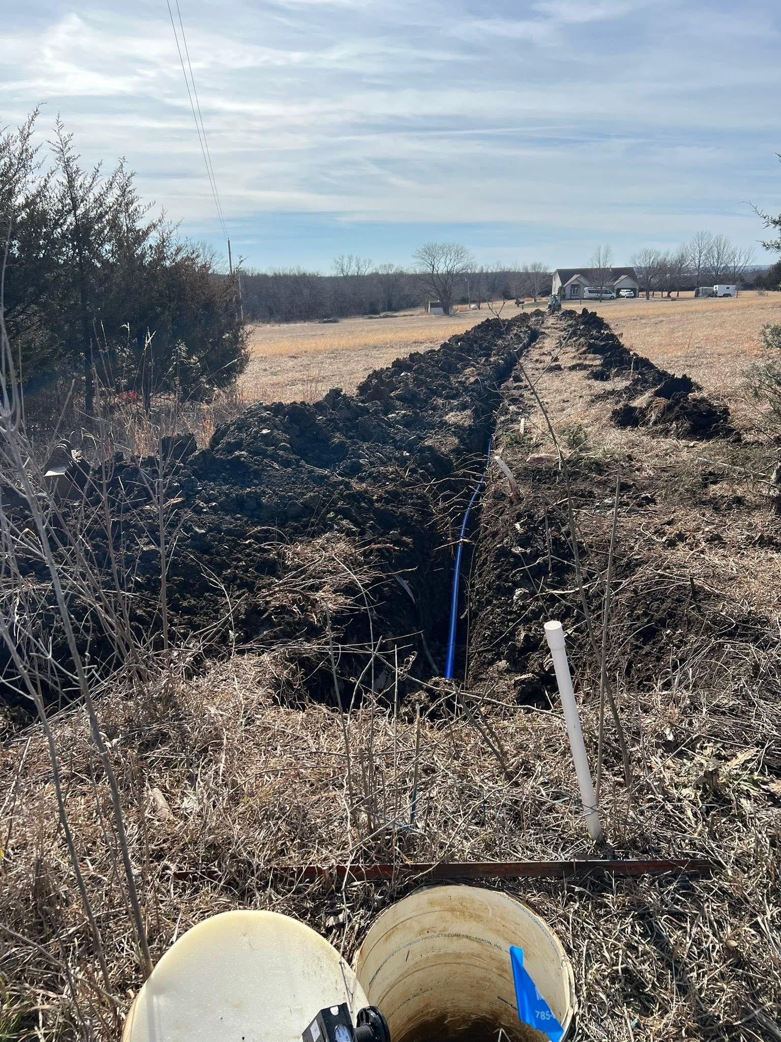 Charred irrigation pipes in a dry field with two pale helmets in the foreground under a clear sky