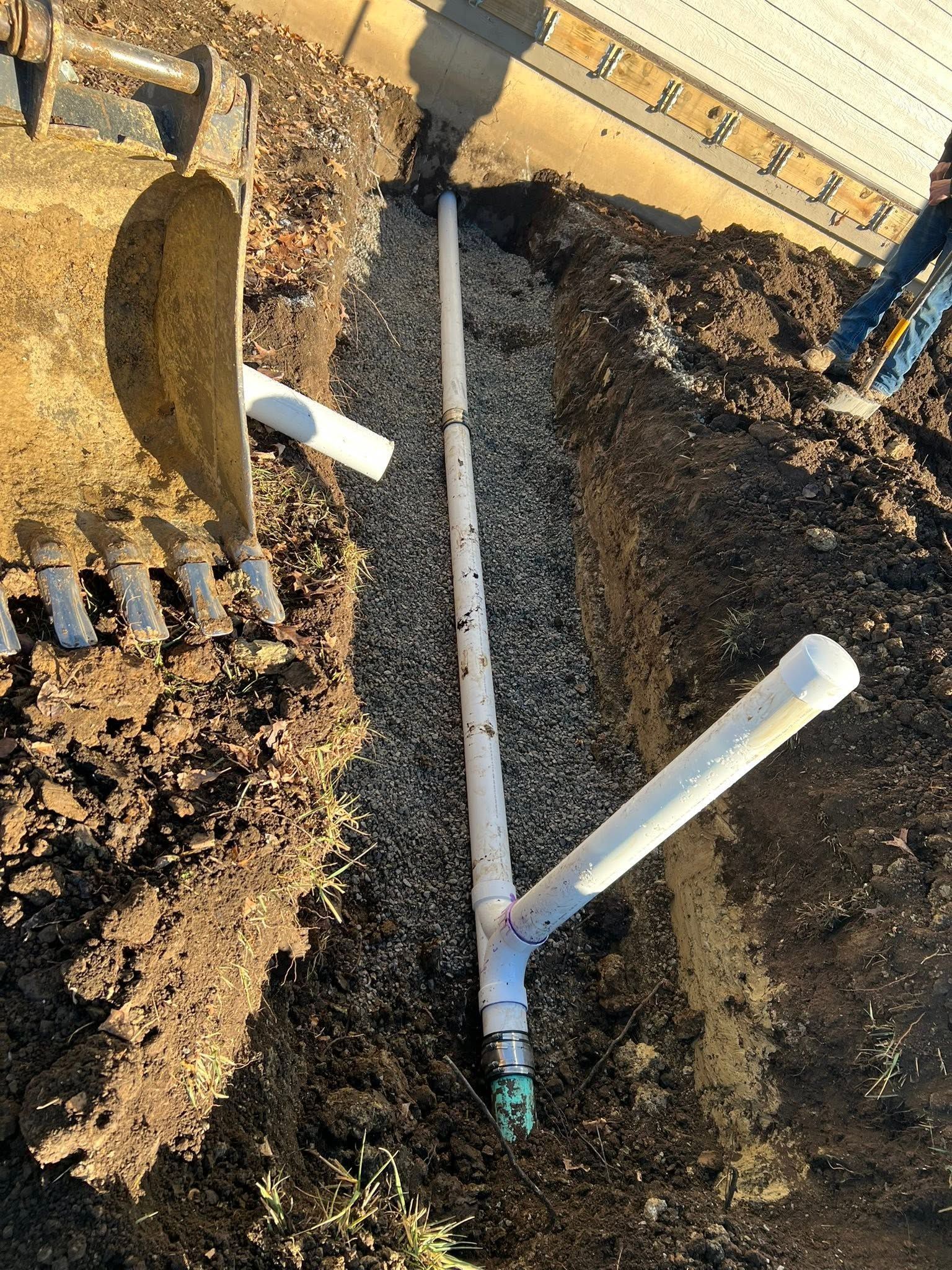 Trenched PVC pipes and a shovel beside a residential foundation during plumbing work