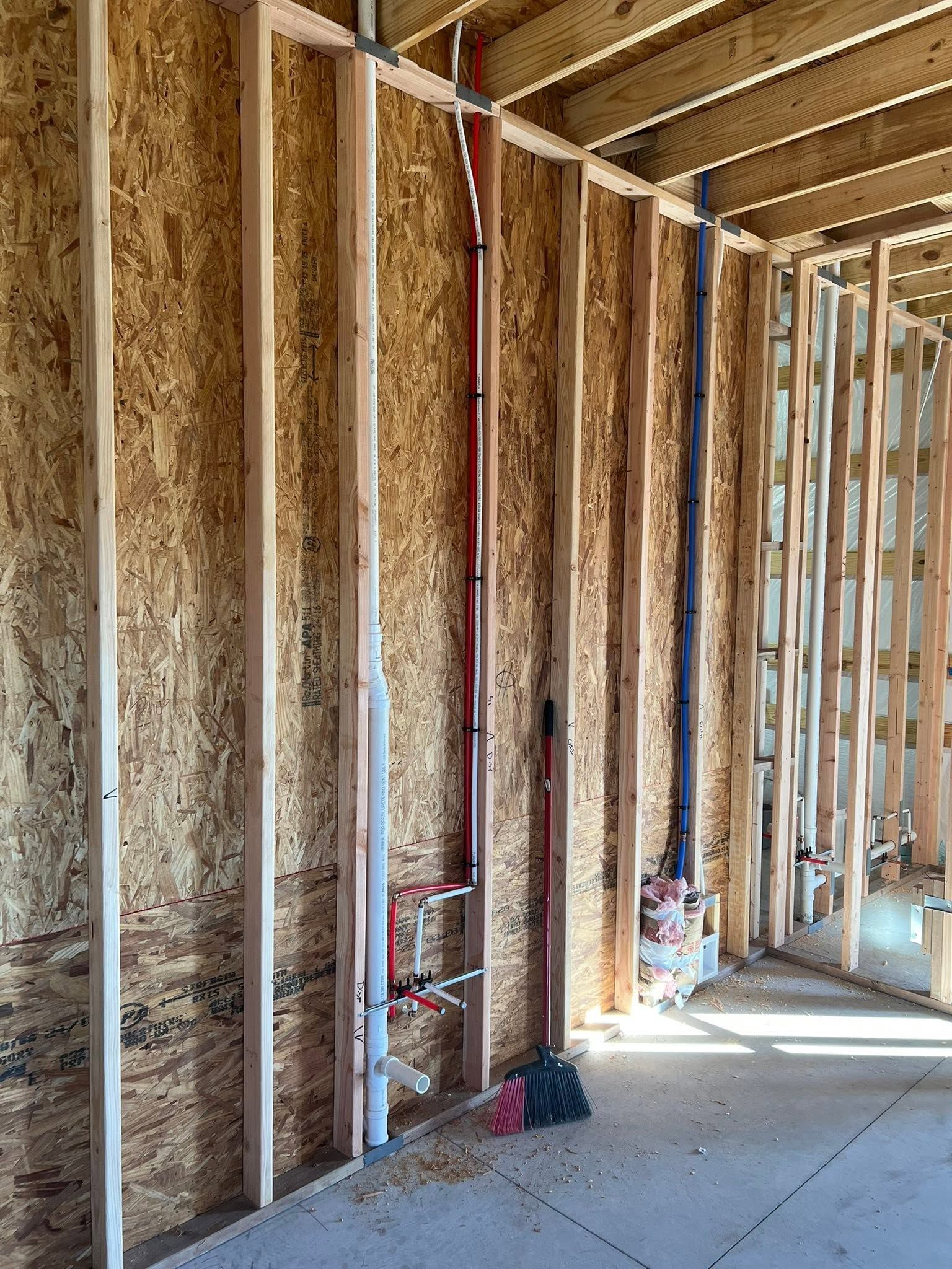 Unfinished interior wall with exposed insulation and wooden studs, showing a construction site floor.