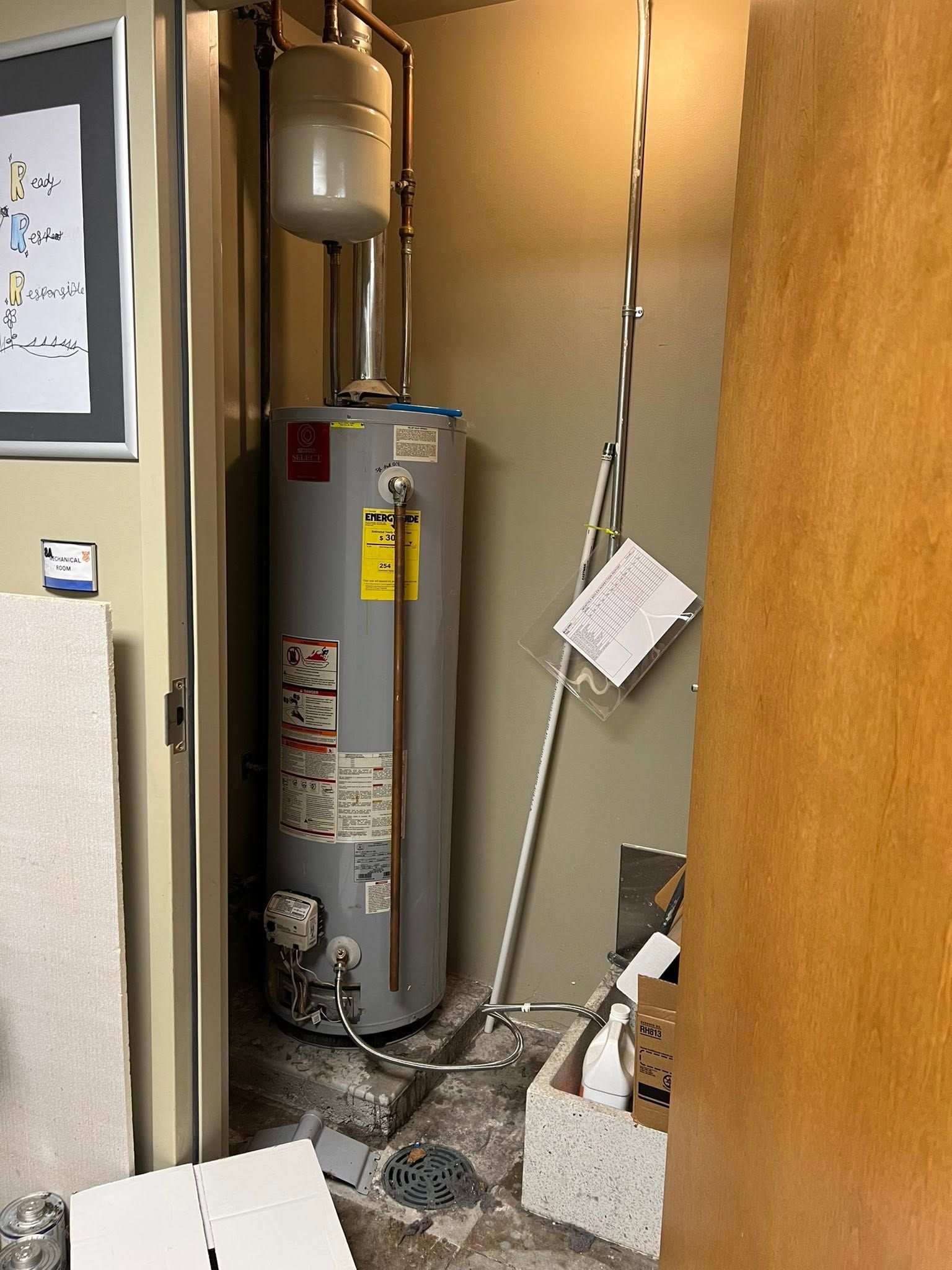 Water heater in a utility closet with exposed pipes and debris on the floor.