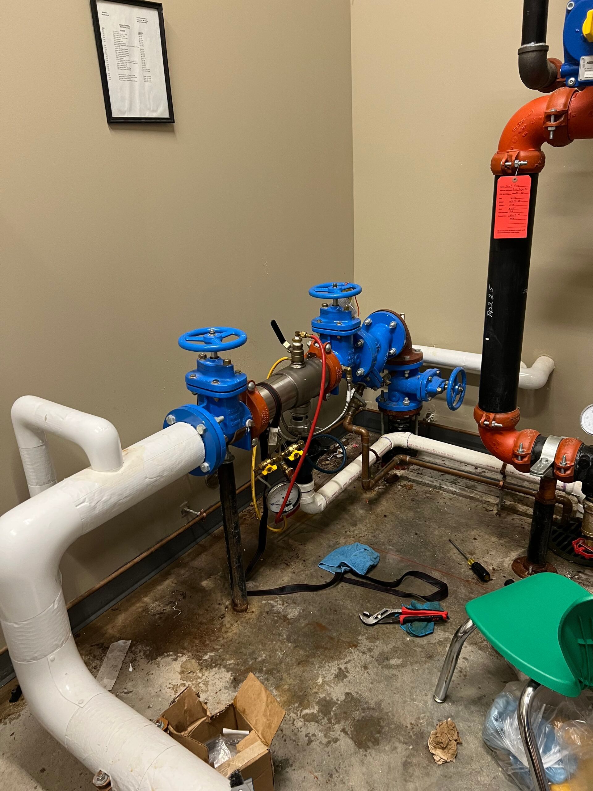 Commercial plumbing with blue valves and white/orange pipes in a utility room, with tools on the floor