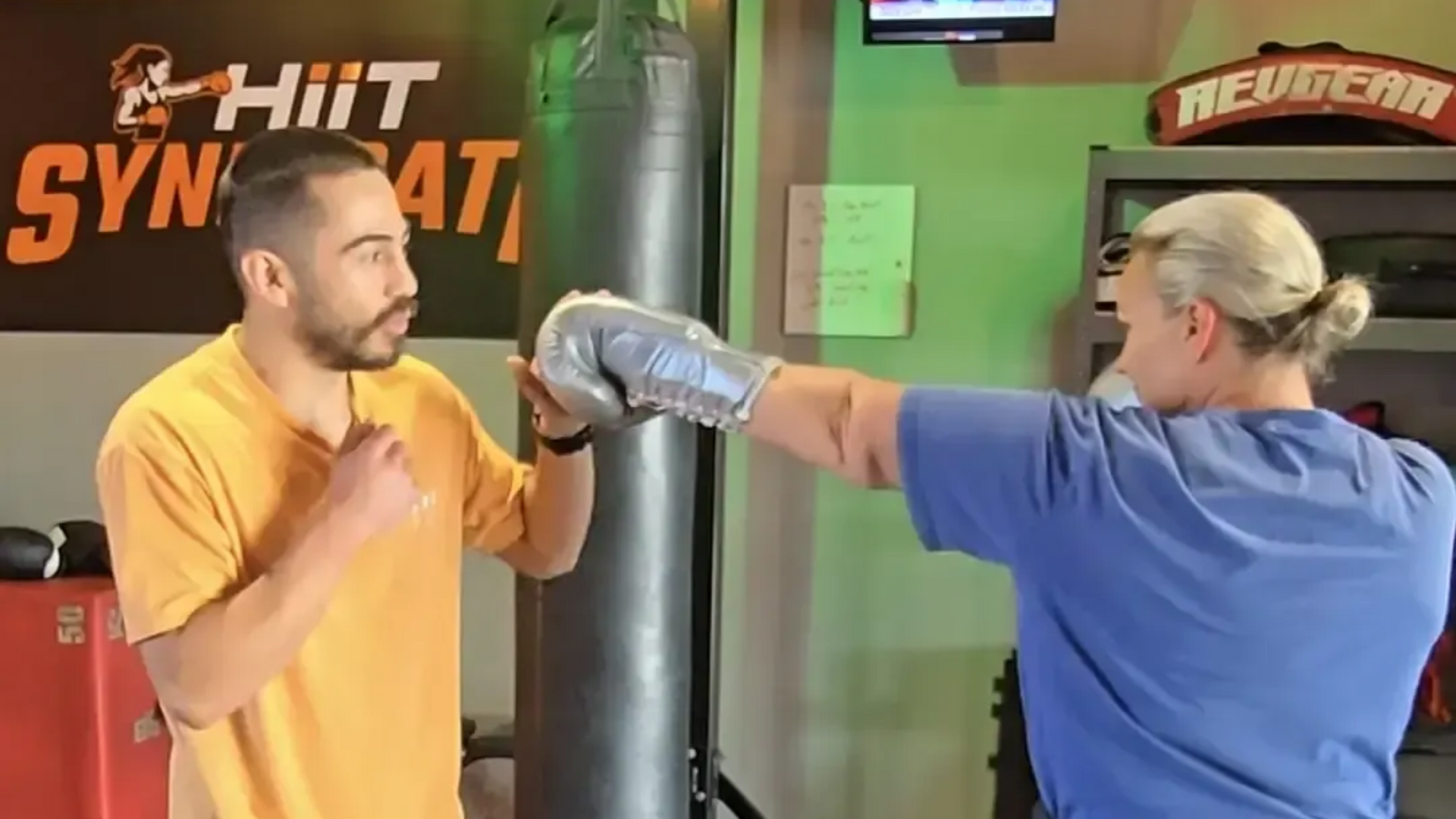 Boxer in black gloves practices punches with a trainer in a gym.