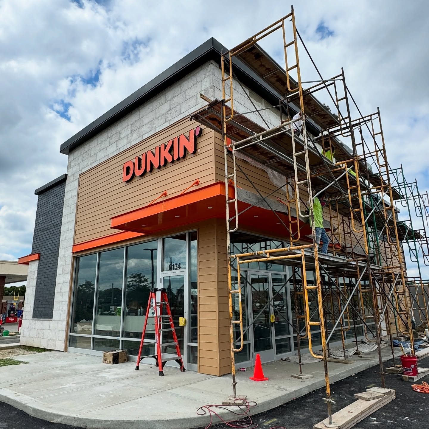 Dunkin’ storefront under construction with scaffolding, ladders, and orange awning