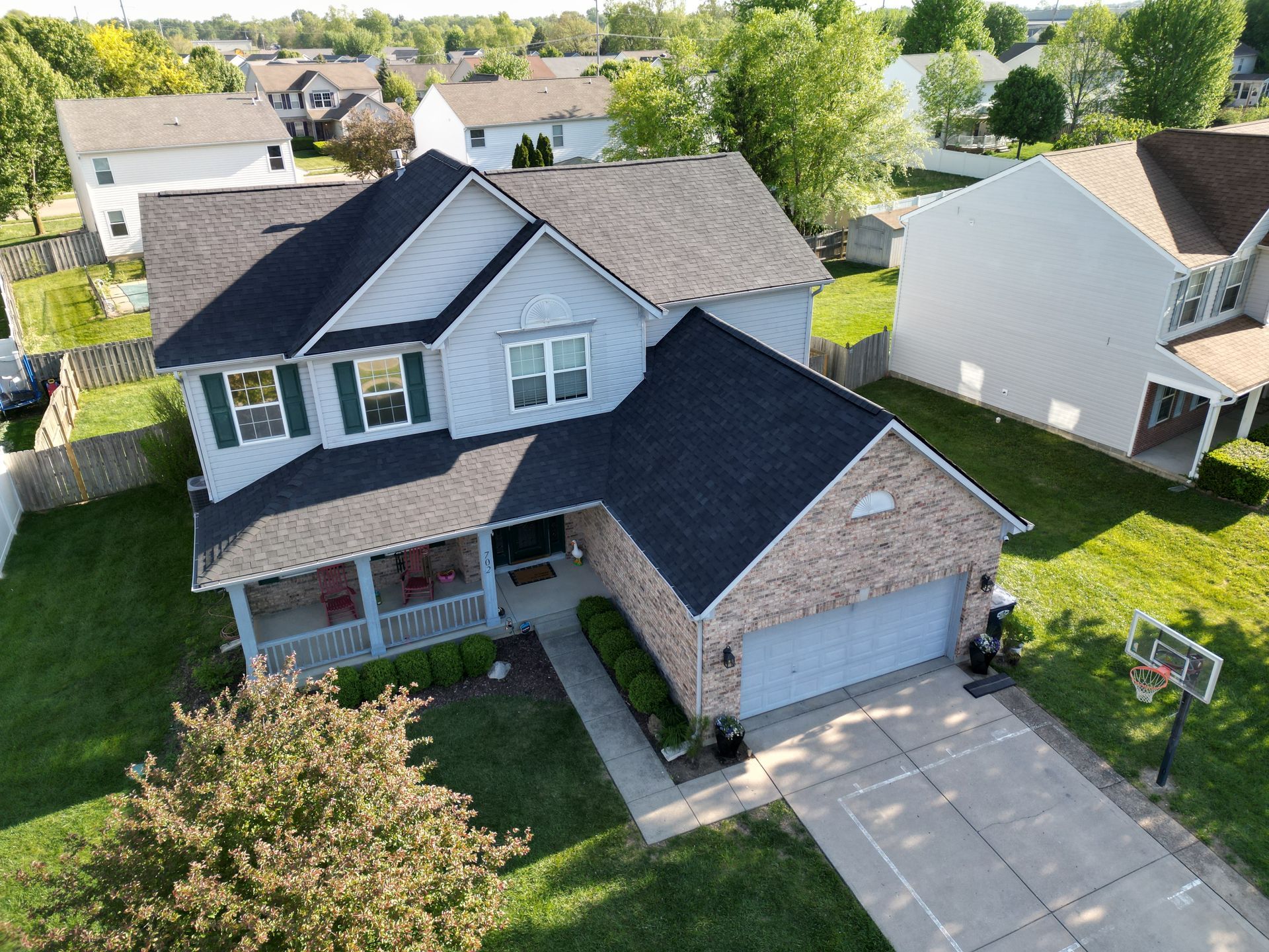 Aerial view of a two-story suburban house with a gray roof, brick facade, driveway, and basketball hoop.