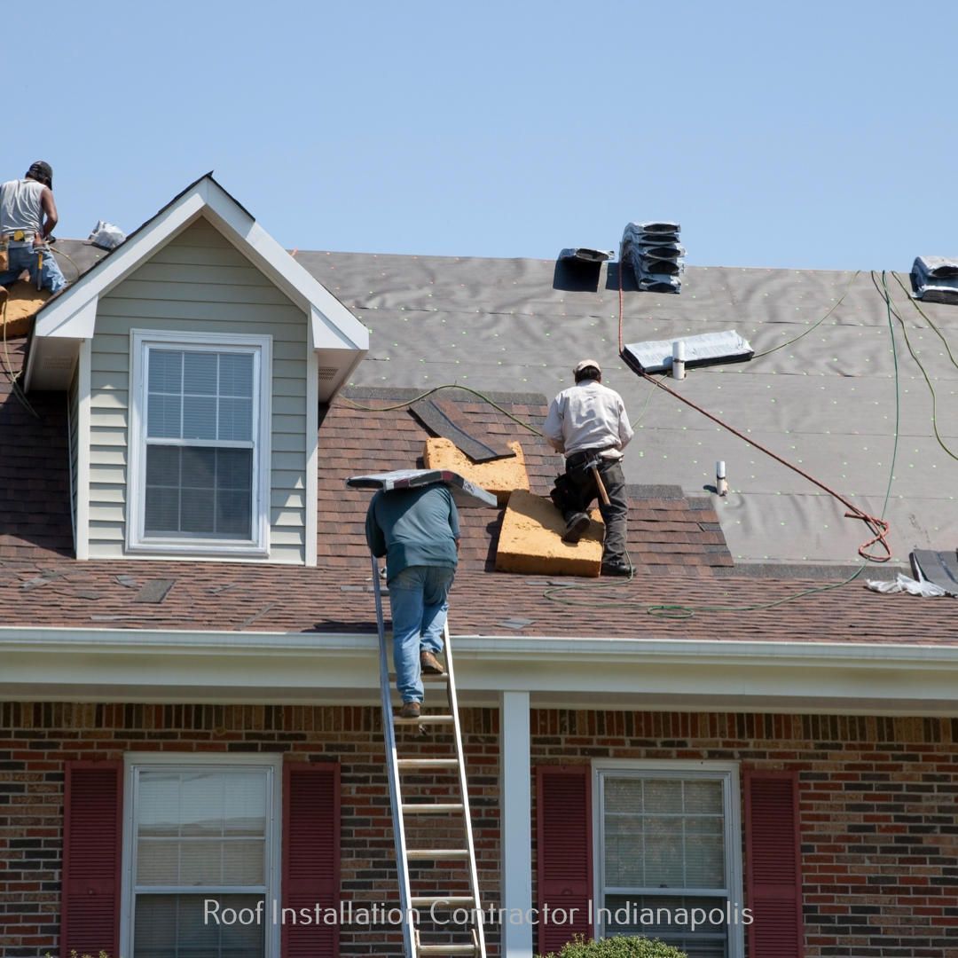 Three workers install shingles on a residential roof with a brick facade and a dormer window under a clear blue sky.