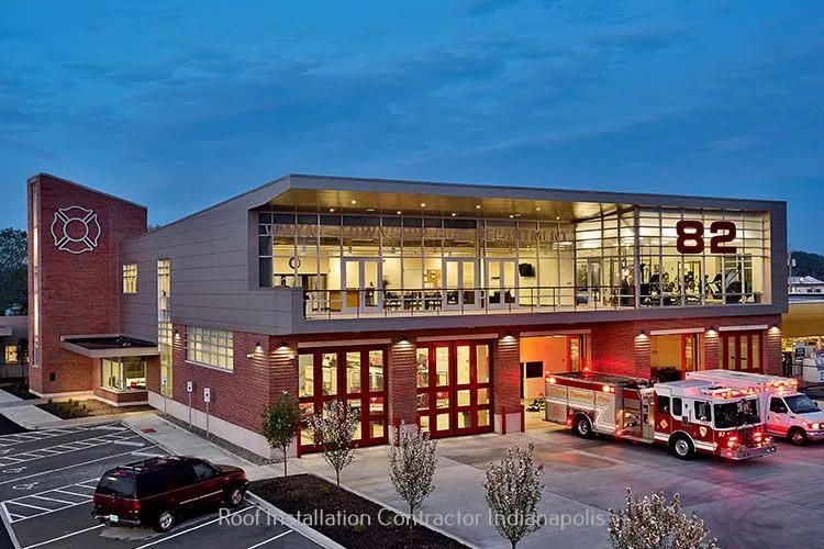 Modern brick and glass fire station numbered 82 at dusk, with fire trucks parked in the bay and a car in the foreground.