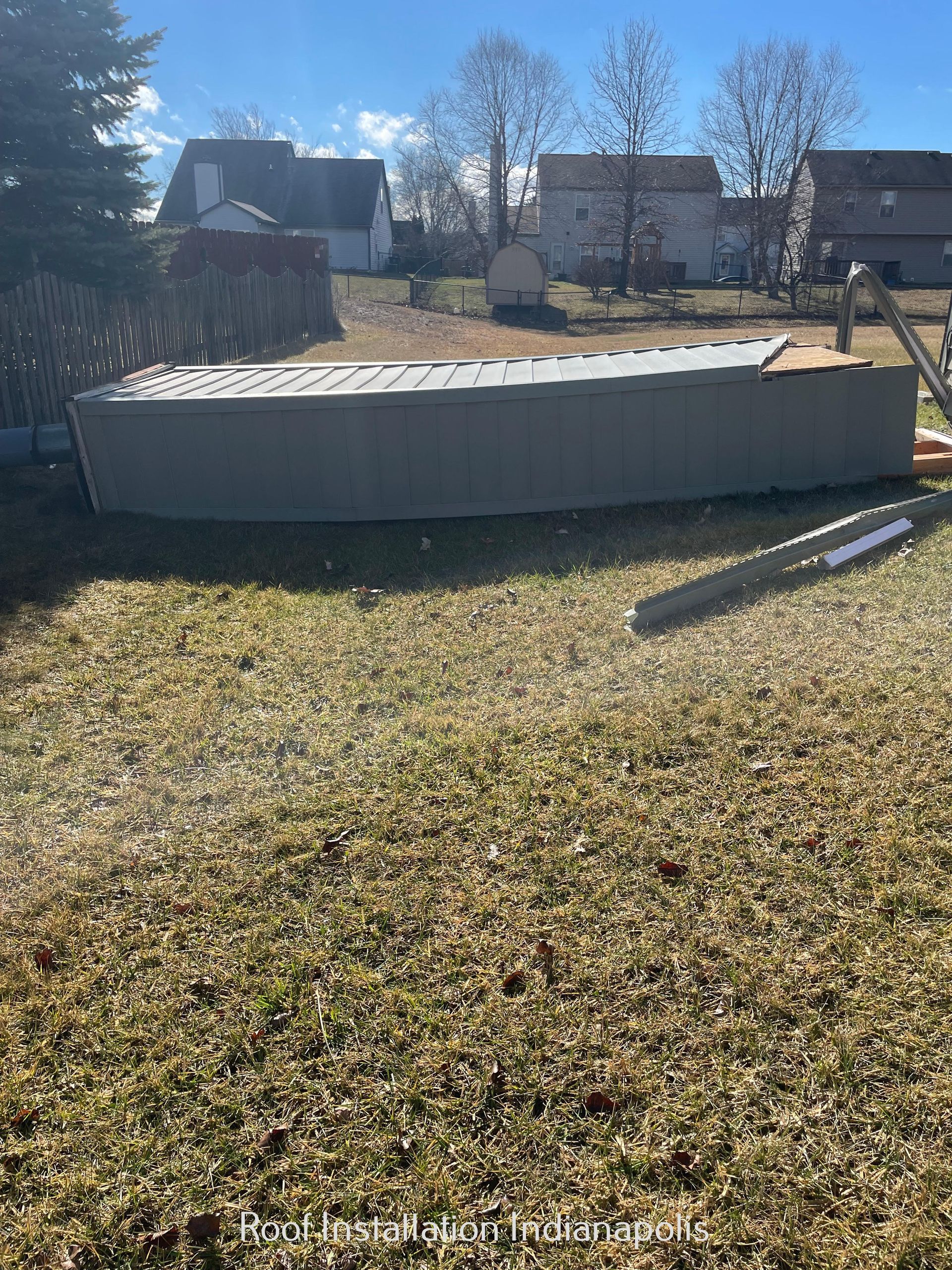 A metal shed lying on its side in a grassy backyard on a sunny day.