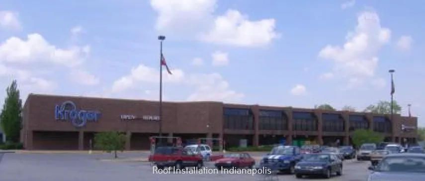 A brown brick Kroger grocery store building with a parking lot and several parked cars under a blue sky.