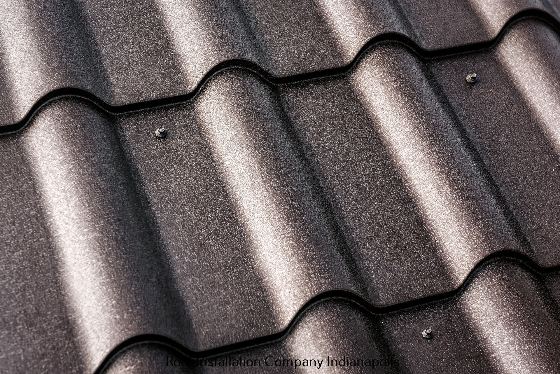 A close-up view of dark brown, textured metal roof tiles with visible mounting screws.