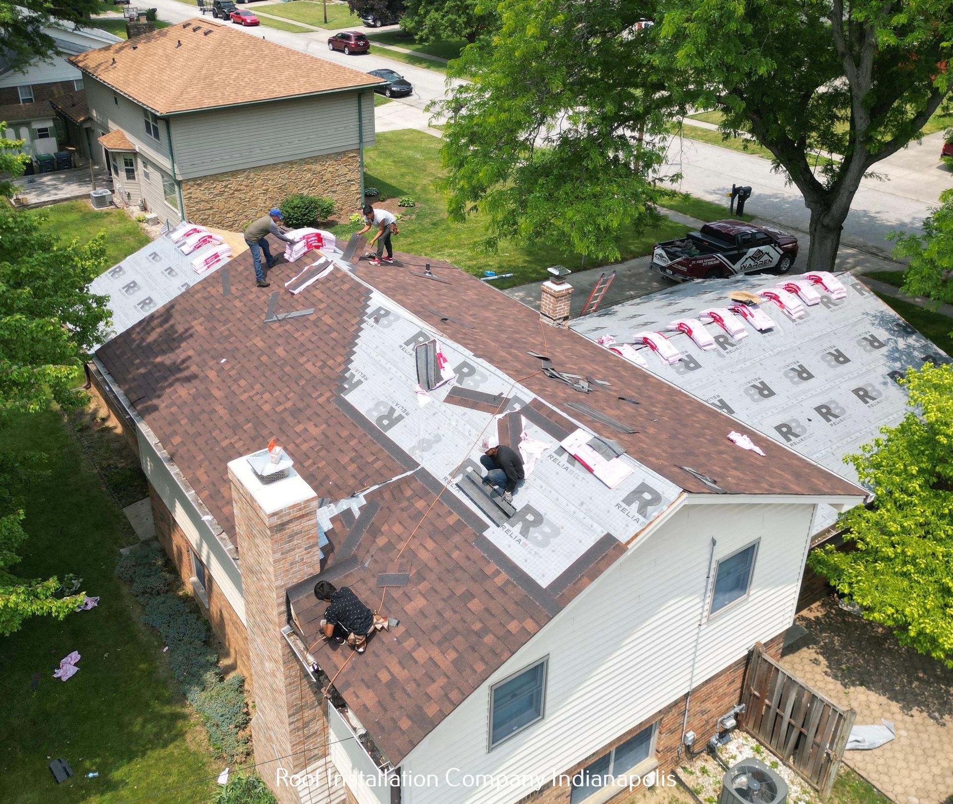 Workers installing brown shingles on a house roof on a sunny day.
