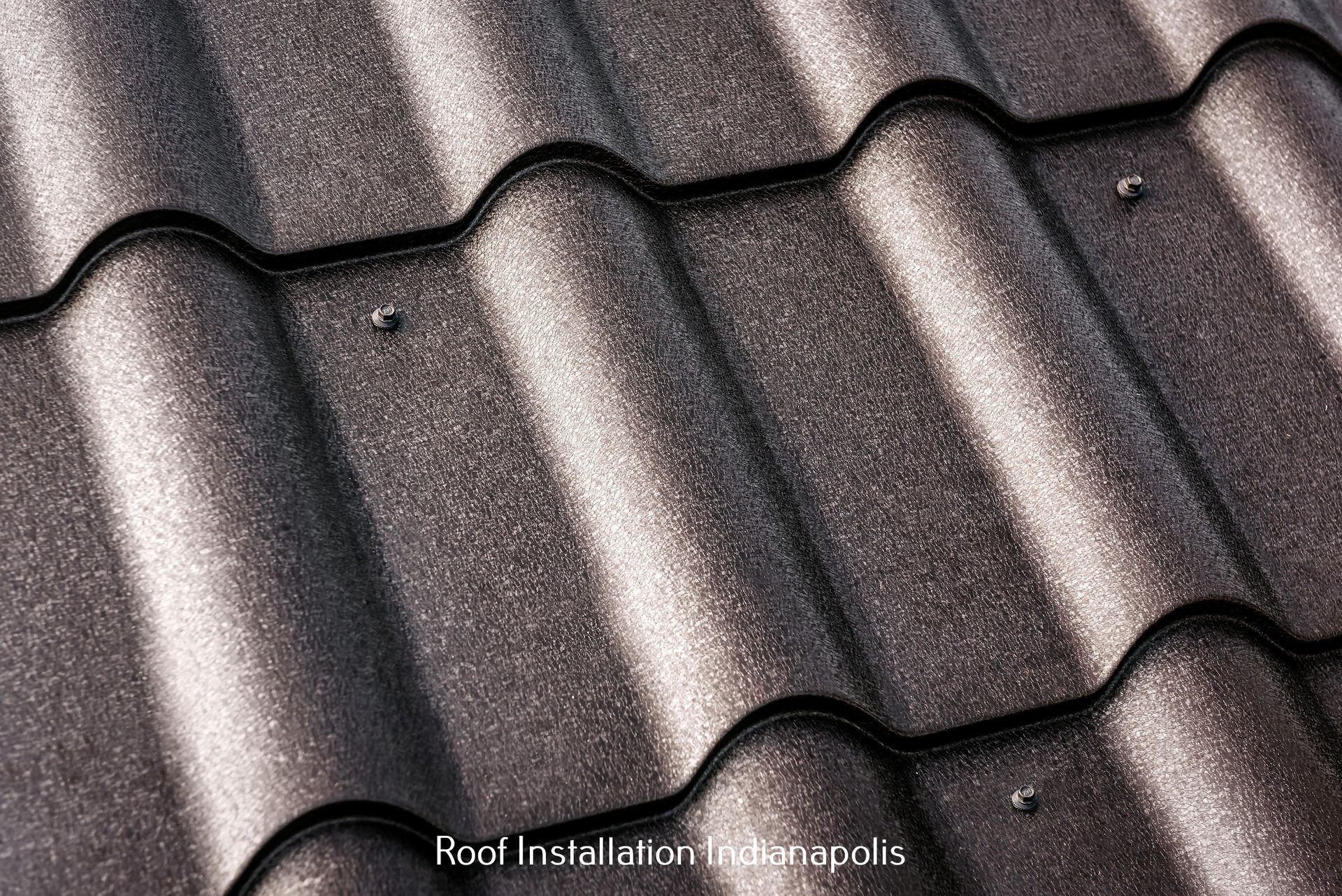 Close-up of a textured, dark gray metal roof tile system with visible screw fasteners.