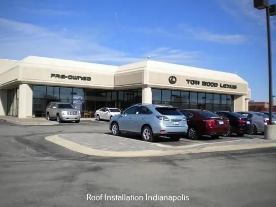 Tom Wood Lexus dealership building in Indianapolis with several cars parked in front under a clear blue sky.