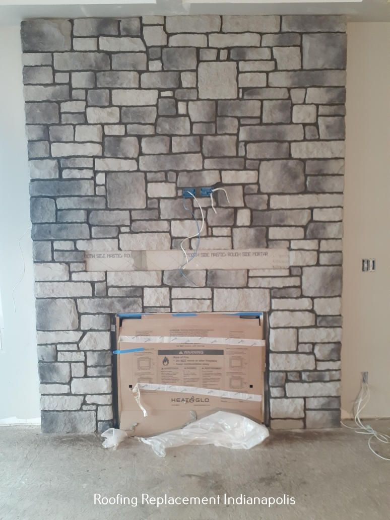 A fireplace installation in progress with a gray-toned faux stone facade and a cardboard-covered firebox.