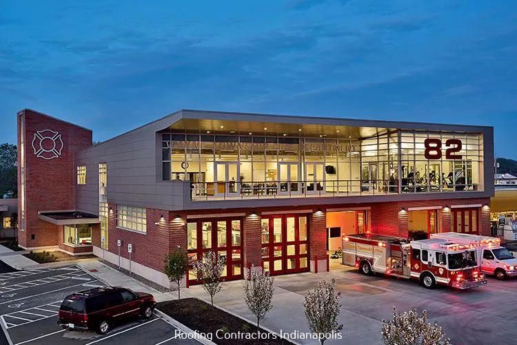 Modern fire station 82 at dusk, featuring a brick and glass exterior, bay doors, and emergency vehicles parked outside.