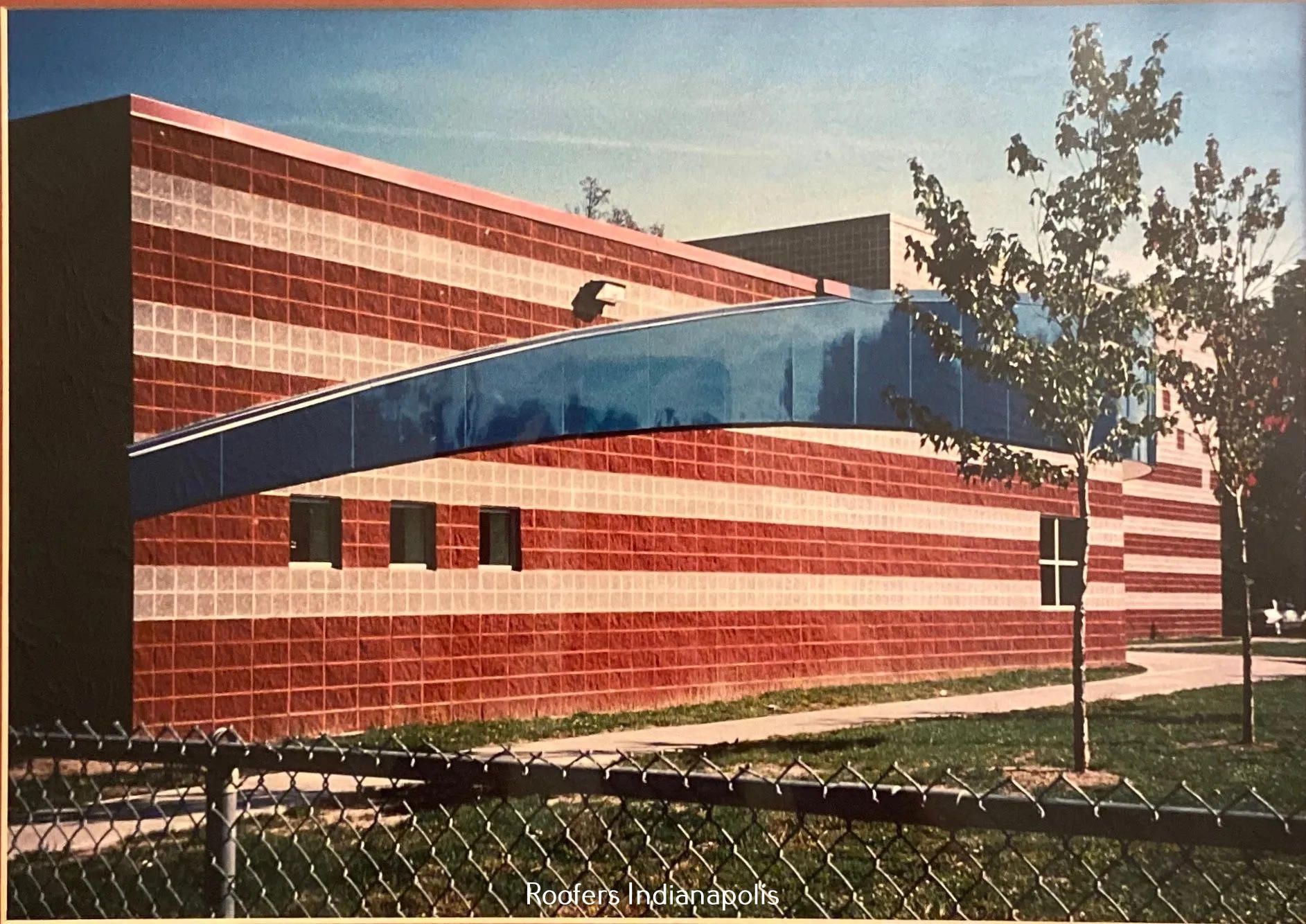 A brick building with alternating red and white stripes and a curved blue overhang, set against a clear sky.