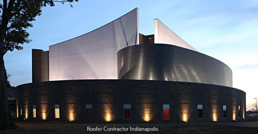 A modern building at twilight featuring a curved stone base with lit windows and striking, angular metal upper structures.