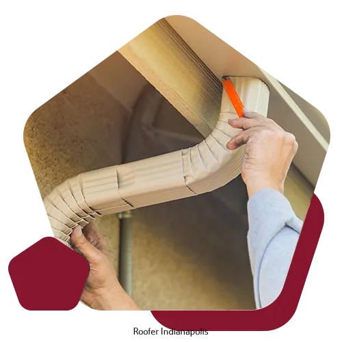 A worker installs a metal downspout onto the side of a building, using a tool to secure it to the eave.