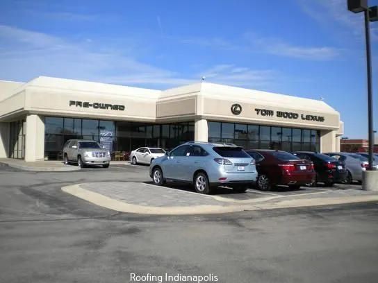 The Tom Wood Lexus dealership building in Indianapolis with several cars parked in the front lot under a blue sky.