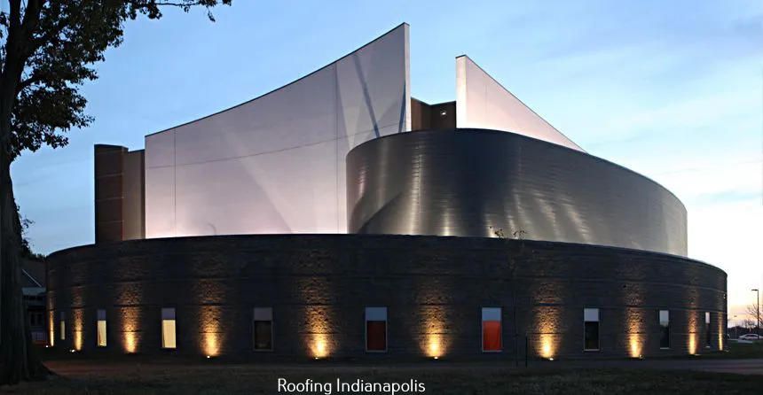 Modern building with a curved stone base, illuminated by ground lights, topped by soaring, angular white and metal walls.