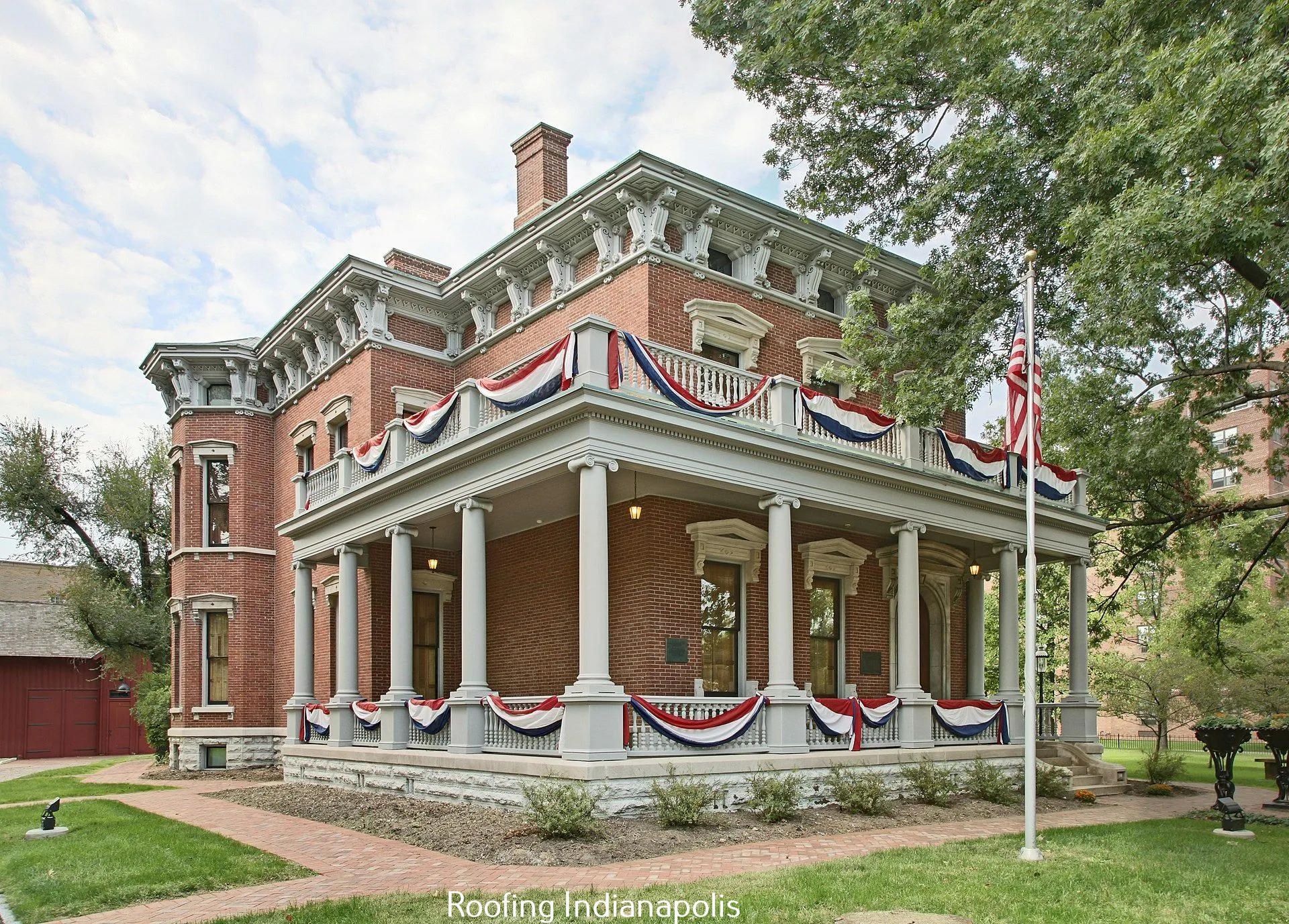 A historic brick Italianate house in Indianapolis with a wrap-around porch adorned with patriotic red, white, and blue bunt.
