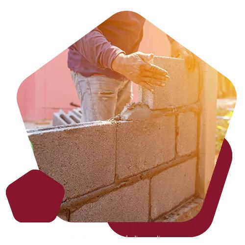 A person laying gray concrete blocks to build a wall, with sunlight casting a warm glow.