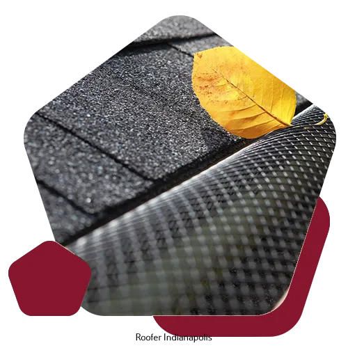 A yellow leaf rests on a black mesh gutter guard installed along the edge of a shingled roof.