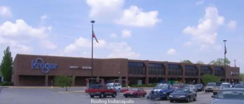 A Kroger grocery store with a brick facade under a partly cloudy sky, featuring a parking lot with several vehicles.