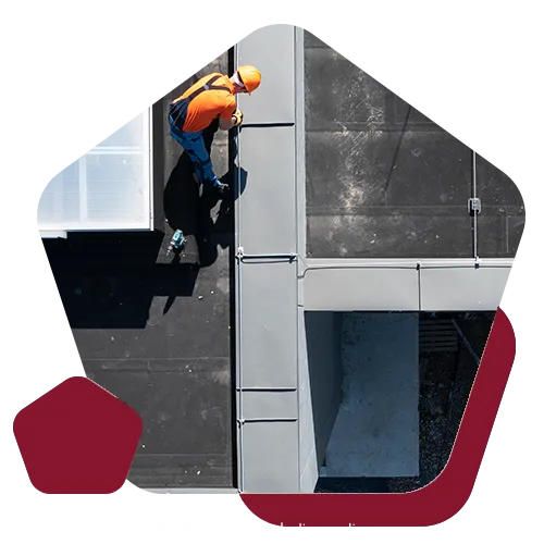 A worker in an orange shirt and hard hat performs maintenance on a flat, dark gray rooftop.