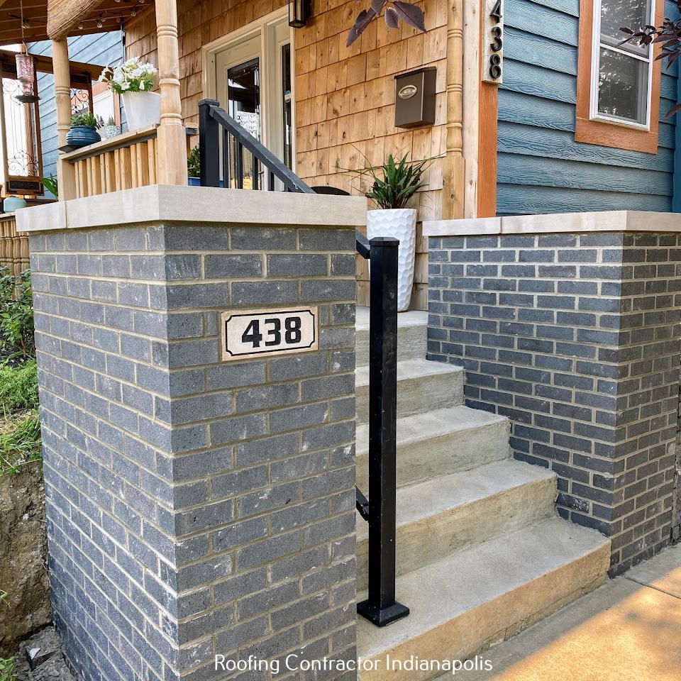 Stone steps lead up to a porch with gray brick walls on either side; a house number