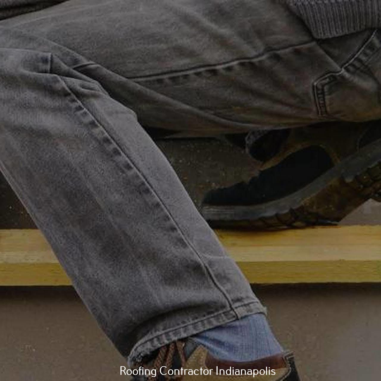 A person wearing gray jeans and brown casual shoes sitting on a wooden surface with a light blue sock visible.