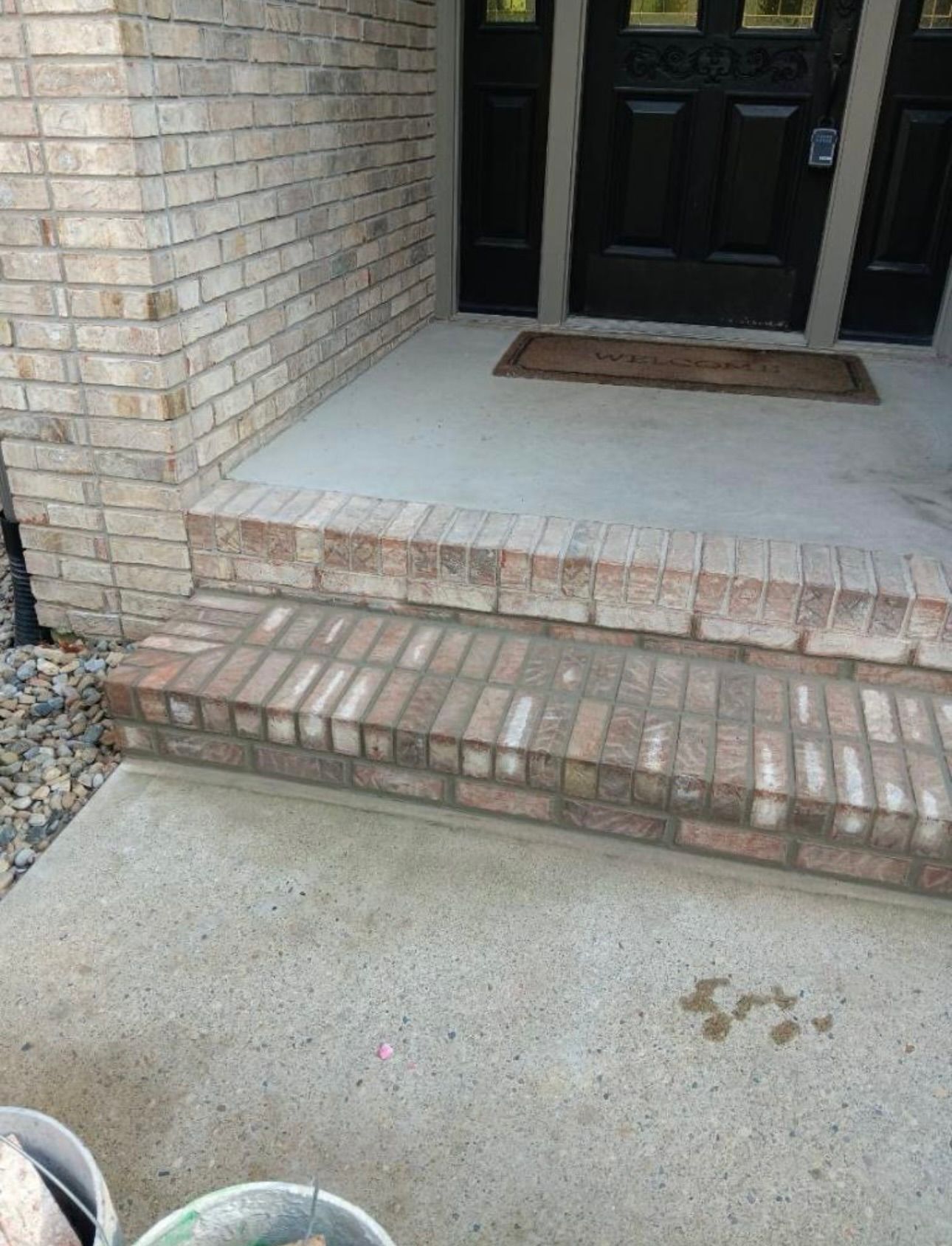 Exterior front porch featuring two brick steps leading up to a concrete entryway with black double doors.