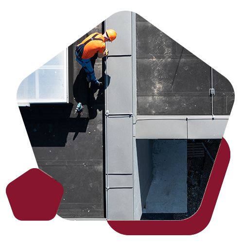 An overhead view of a worker in an orange safety shirt and hard hat working on the roof of a building.