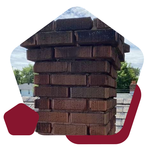 A weathered, dark red brick chimney stack rising from a shingled roof against a clear sky.