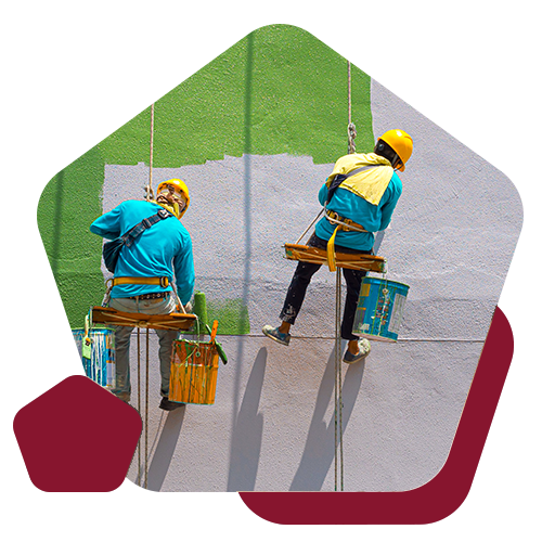 Two workers in safety helmets suspended on ropes paint a large wall, transitioning from green to light purple.