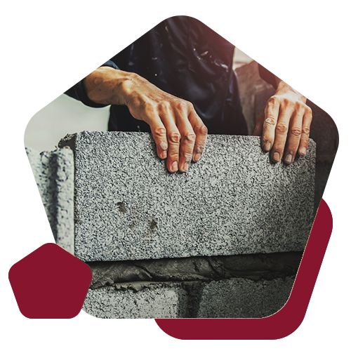 Hands placing a grey concrete block onto a layer of mortar on a construction site.