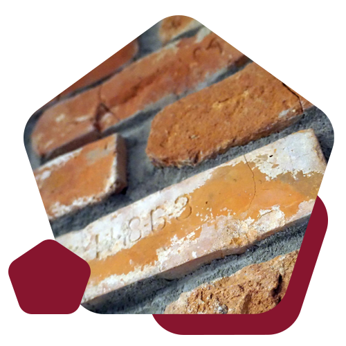 Old, weathered orange bricks are set in a wall; one brick clearly displays the year