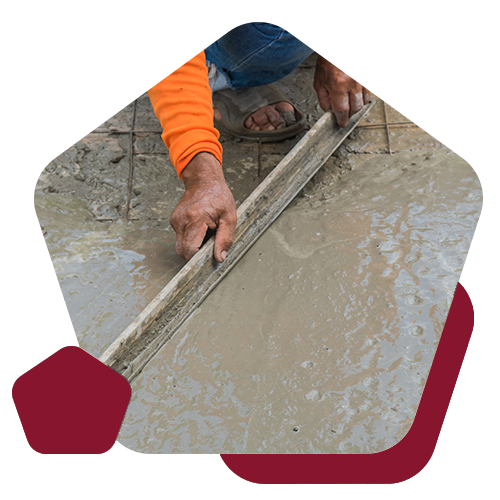 A person wearing an orange long-sleeved shirt uses a metal screed board to level wet concrete.